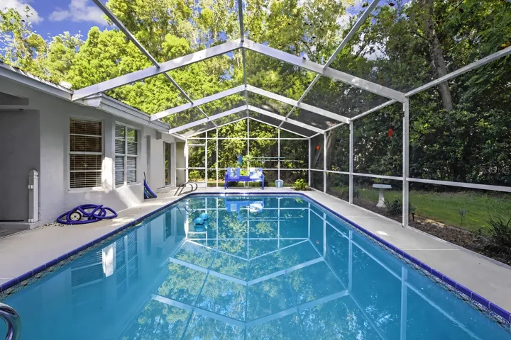 Screen-enclosed swimming pool surrounded by a private wooded setting