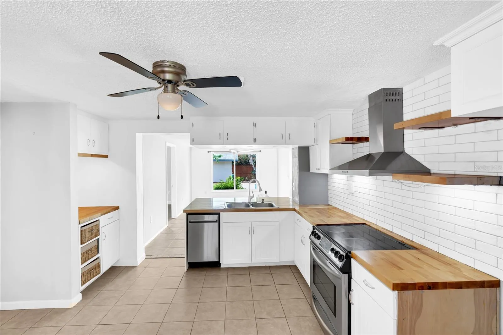 The updated kitchen features white cabinetry, butcher block countertops, stainless steel appliances and a clean subway tile backsplash.