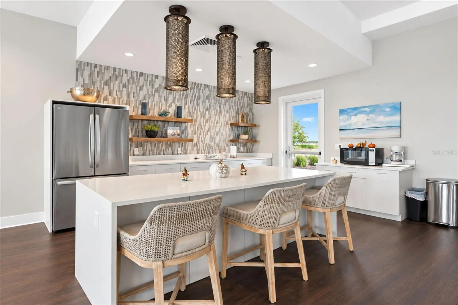 Clubhouse kitchen featuring a spacious island with seating, refrigerator, ice maker, food warmer and microwave—perfect for community gatherings, events and entertaining.
