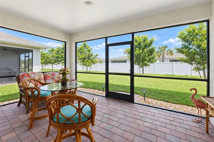 Covered, screened lanai with paver flooring and peaceful green-space views—an inviting spot for morning coffee, outdoor dining or relaxing in the Florida breeze.