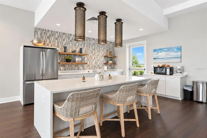 Clubhouse kitchen featuring a spacious island with seating, refrigerator, ice maker, food warmer and microwave—perfect for community gatherings, events and entertaining.