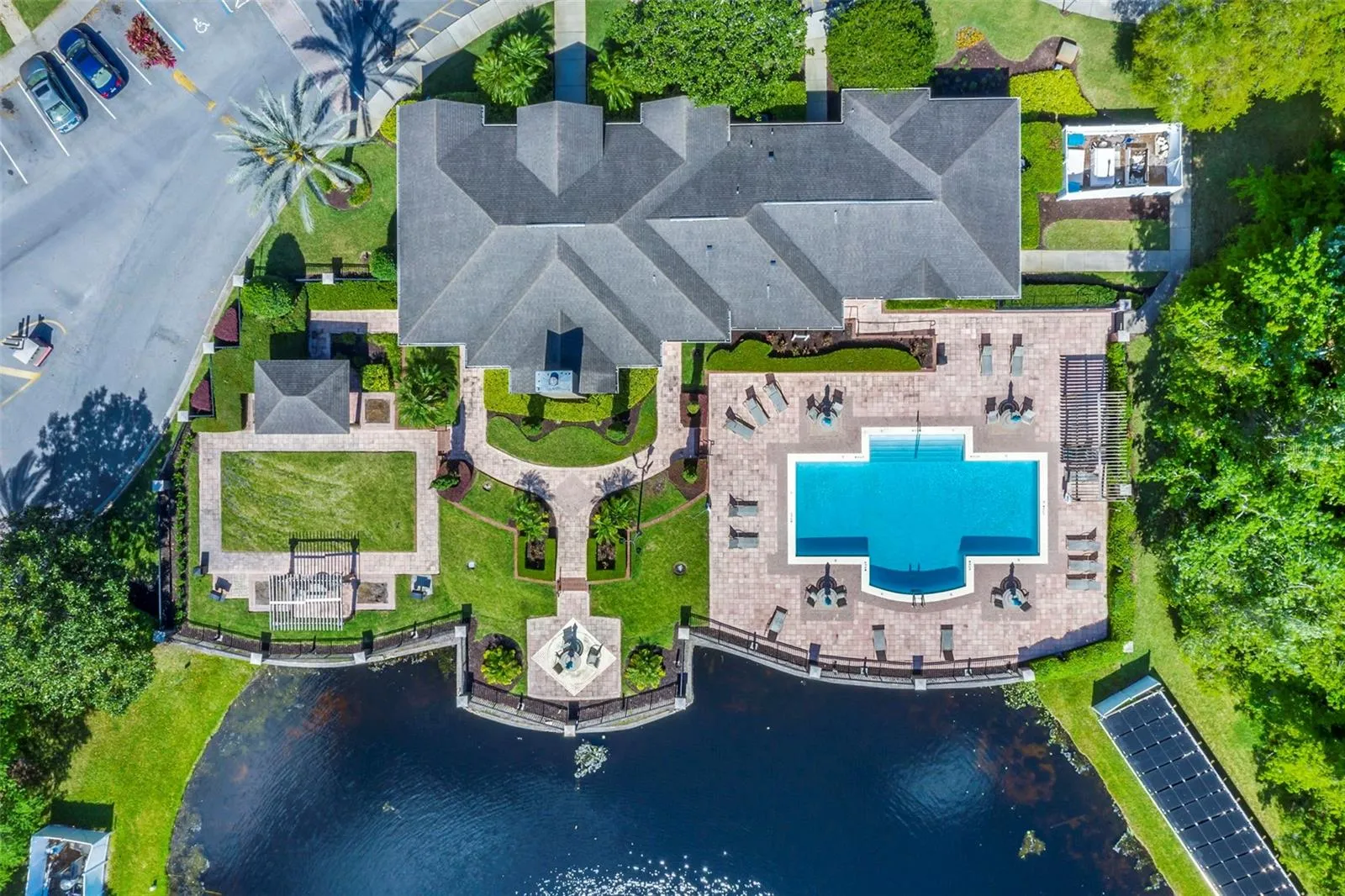 Overhead aerial view of the cross-shaped Sabal Point pool, clubhouse roof, landscaped courtyard, and lake.