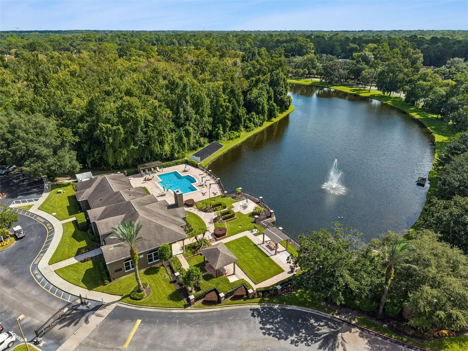 Aerial view of the Sabal Point clubhouse entrance, curved drive, and lakefront pool area with a fountain in the lake.