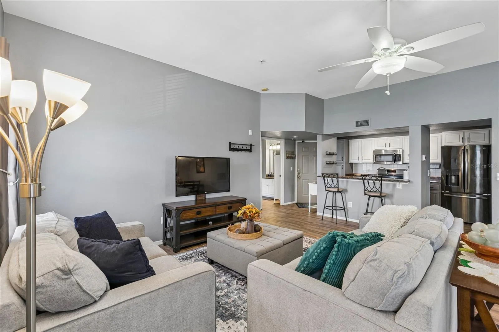 Living room looking toward the kitchen, with the breakfast bar, stainless appliances, and entry foyer visible in the background.