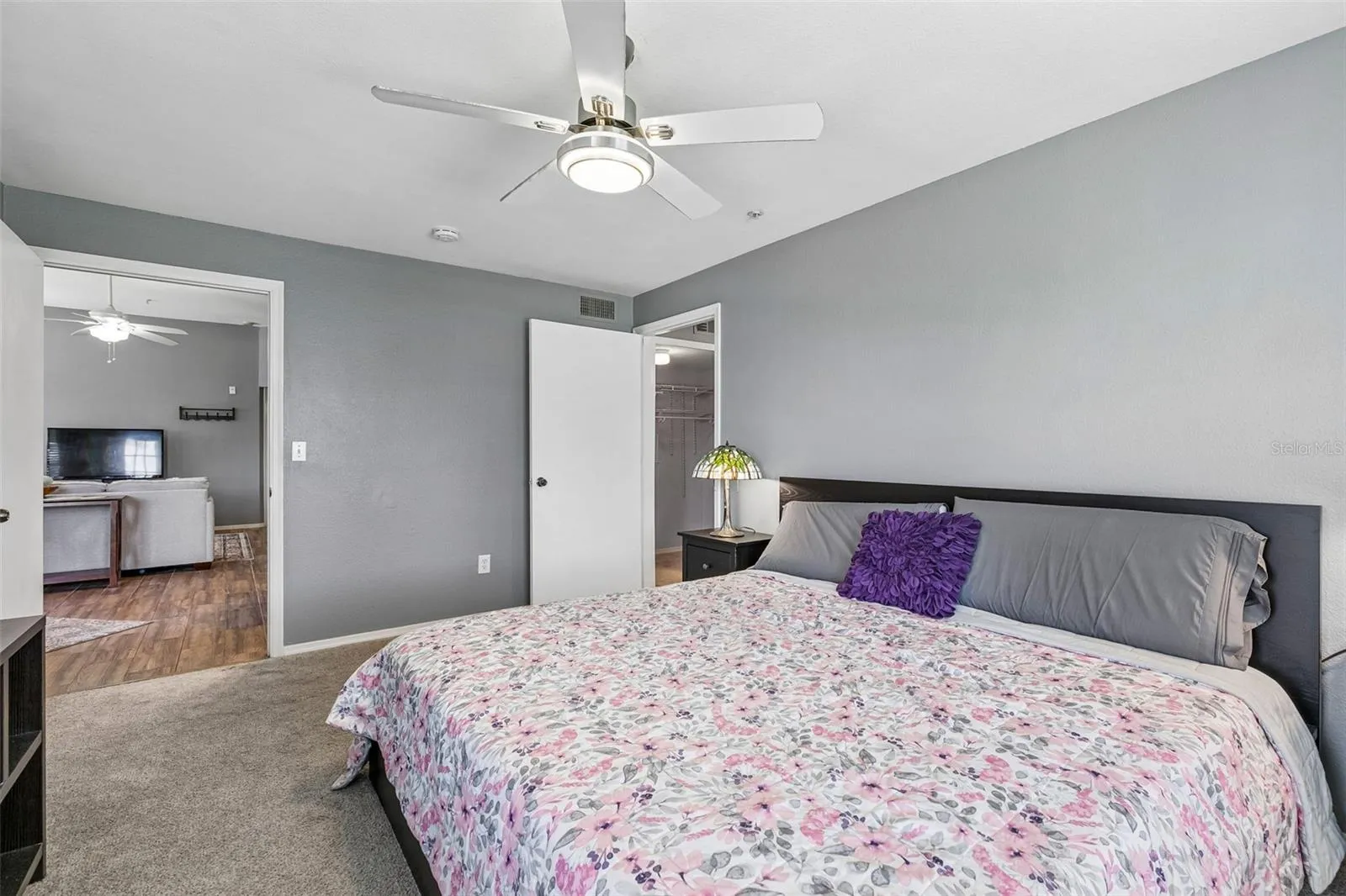 Primary bedroom with a king bed and ceiling fan, with a view through the doorway to the living room.