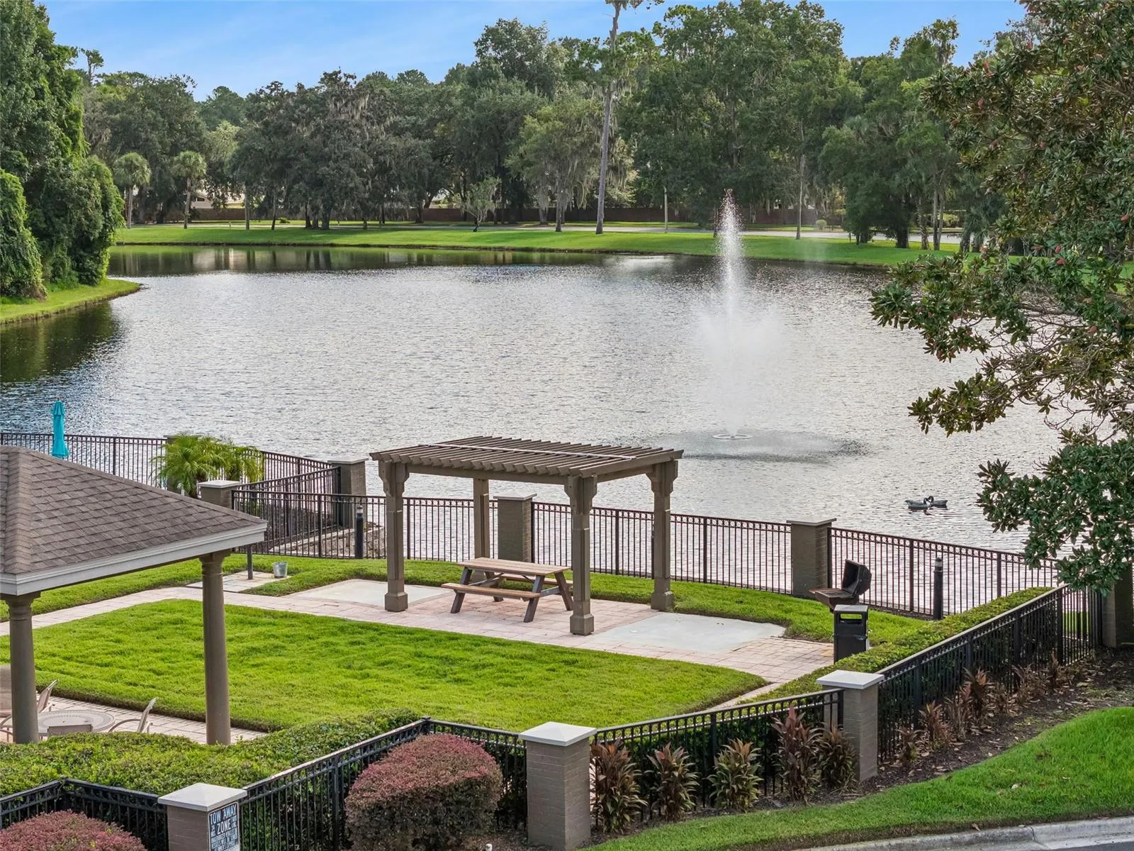 Lakeside gazebo and picnic area at Sabal Point with a manicured lawn, fenced lake edge, and a fountain in the water.