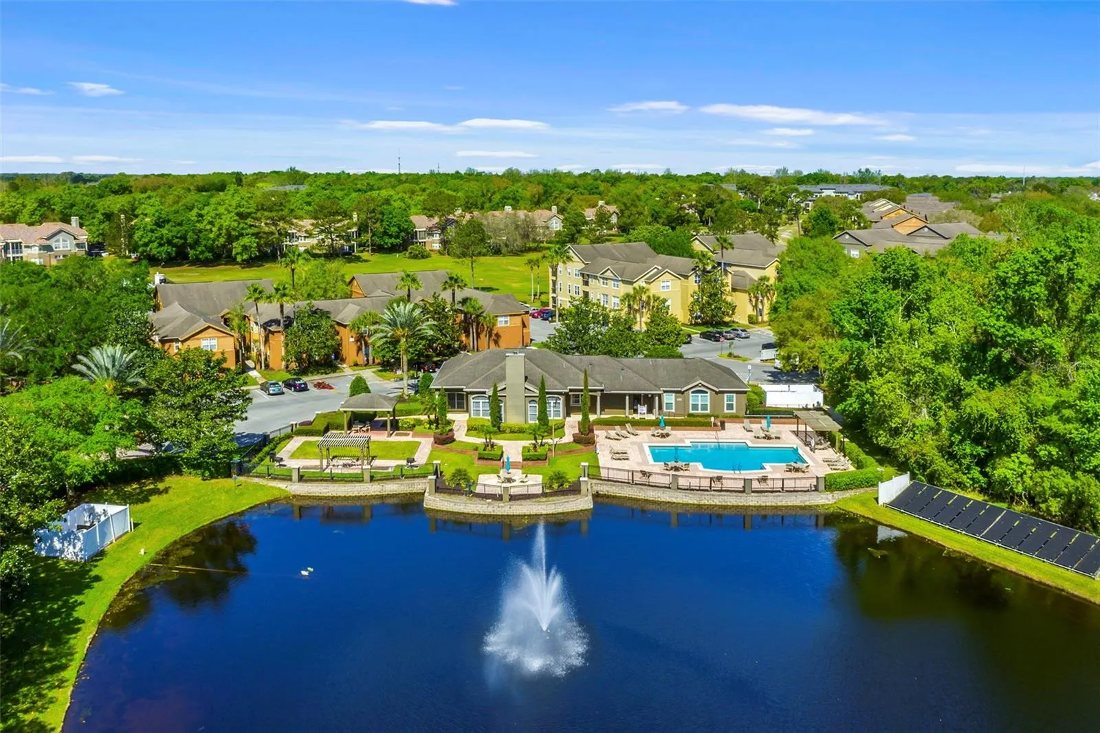 Wide aerial view of the Sabal Point lake with fountain, clubhouse, pool, and nearby residential buildings.