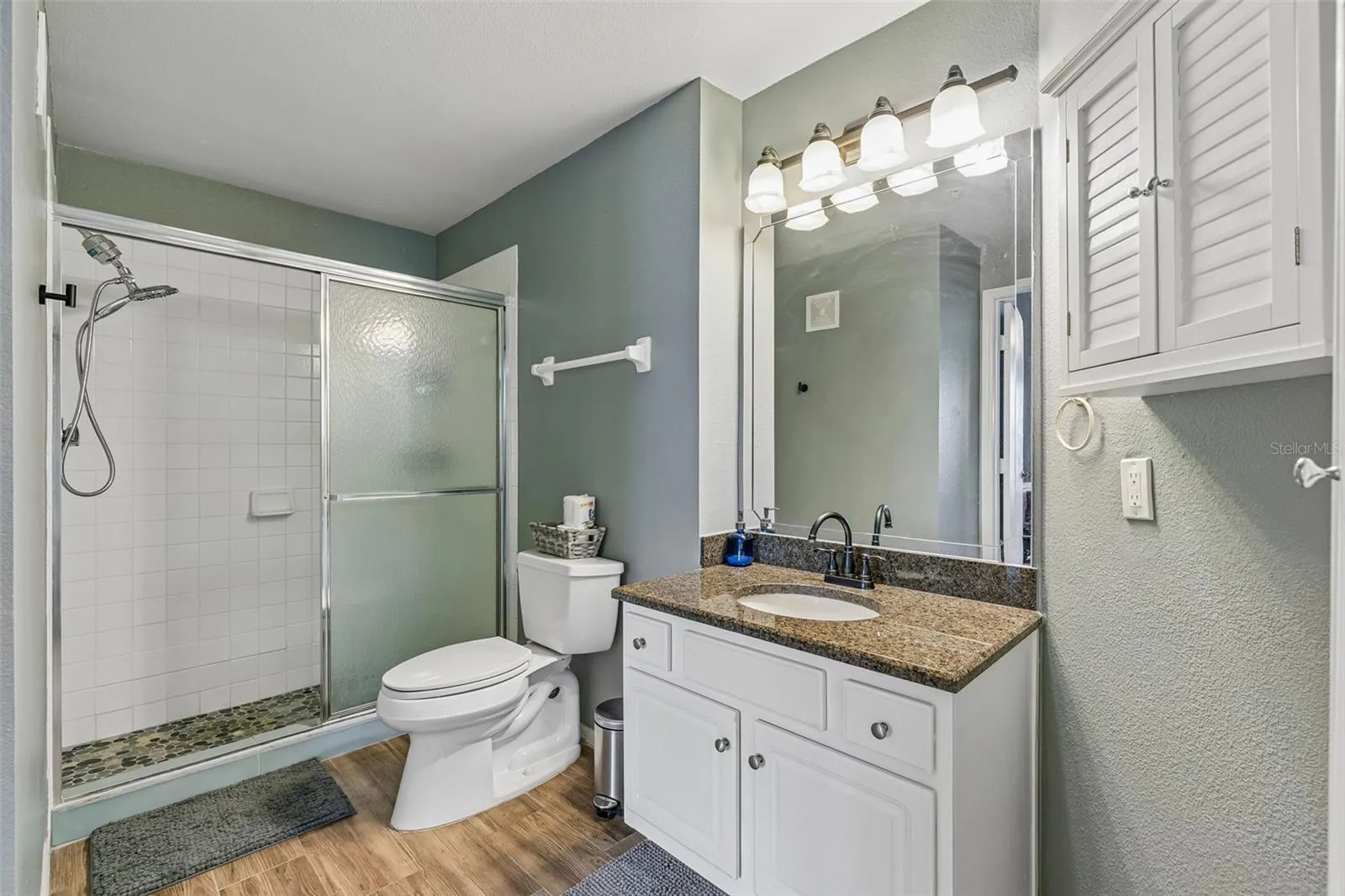 Second bathroom with a granite-top vanity, toilet, walk-in shower with sliding glass door, and a louvered linen cabinet.