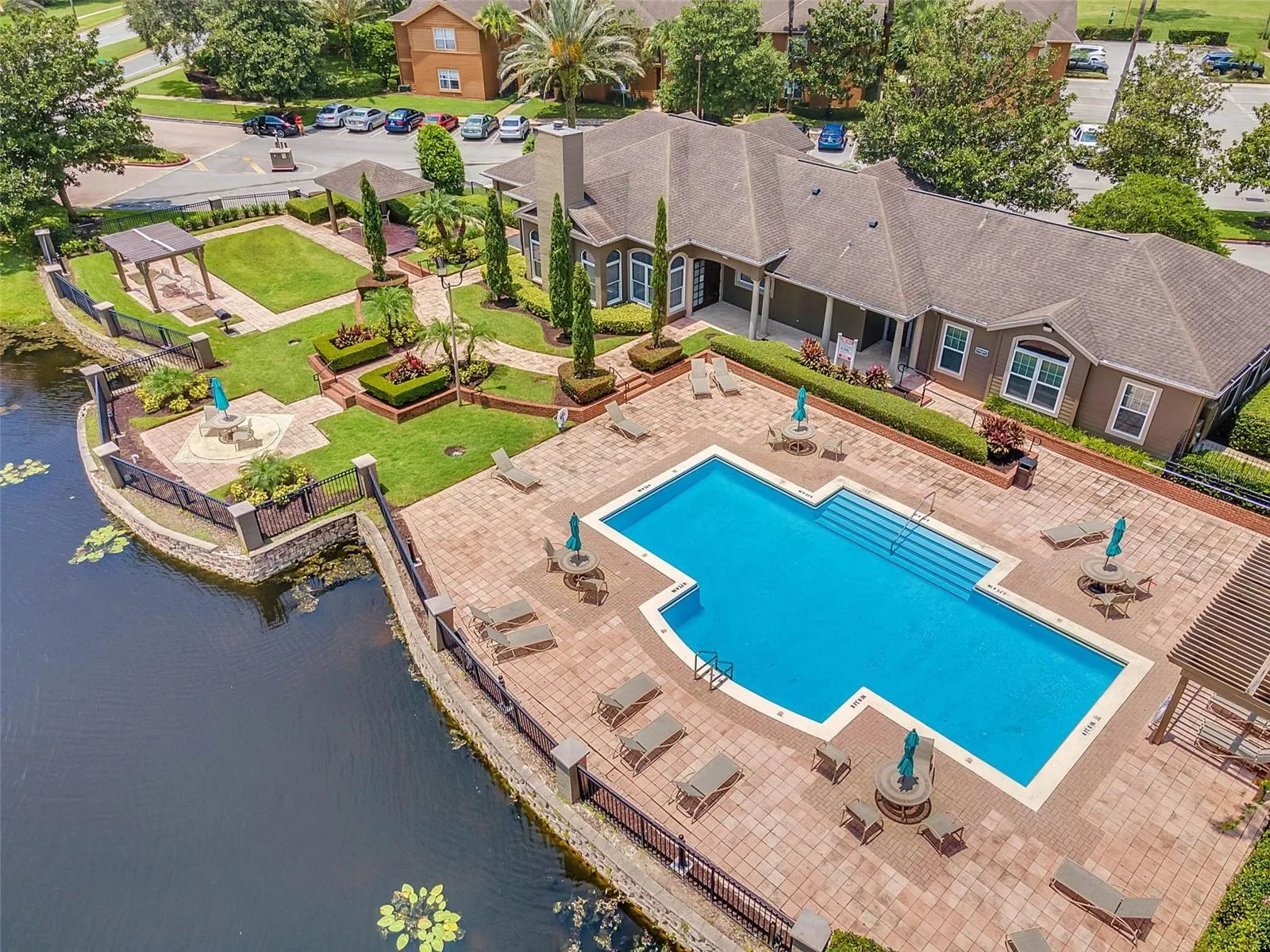 Angled aerial view of the Sabal Point pool, paver deck with lounge chairs, clubhouse, and lakeside courtyard.