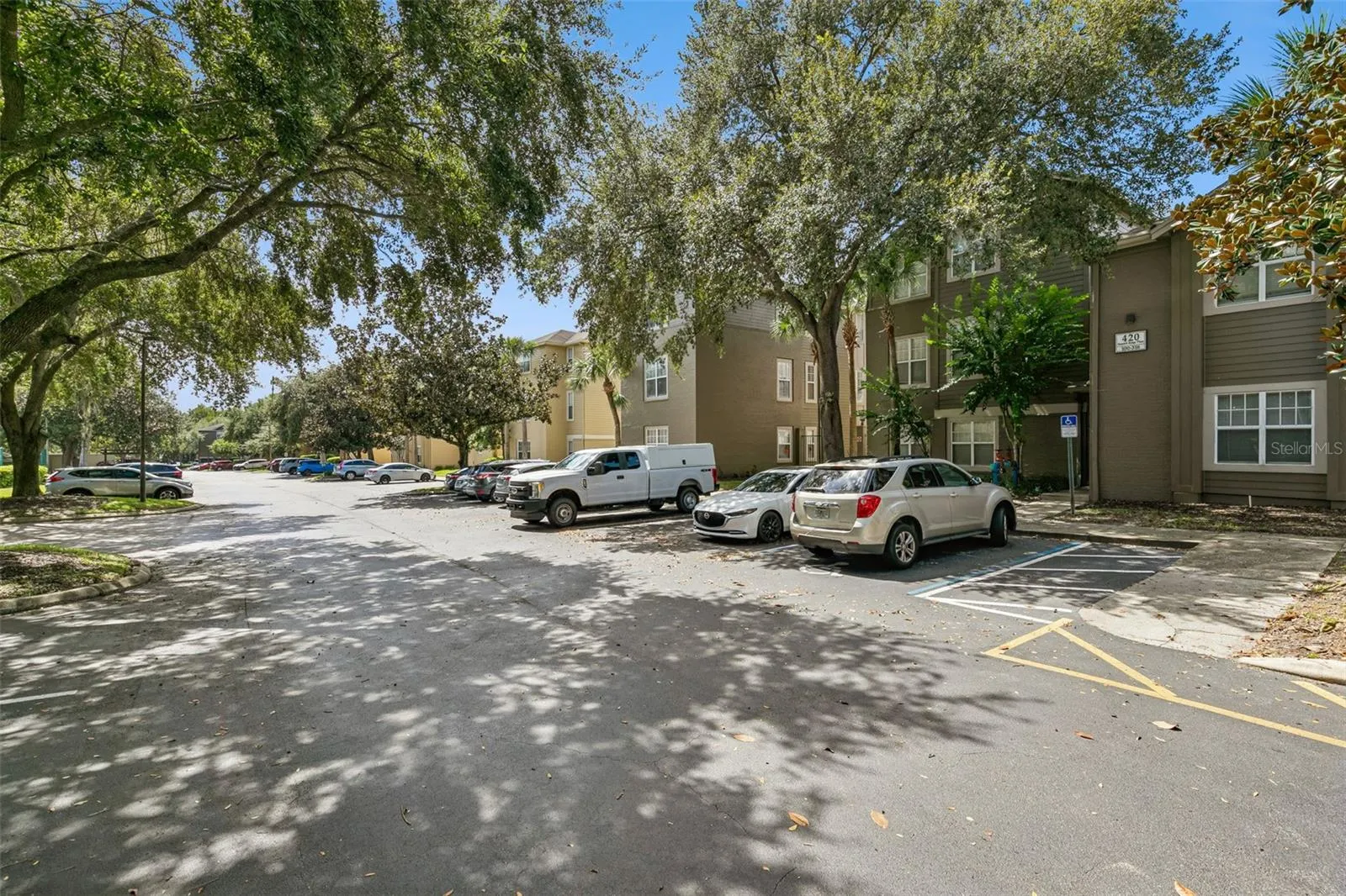 Street-level view of the building and parking lot at Summit Ridge Place in Longwood, FL, shaded by large live oak trees