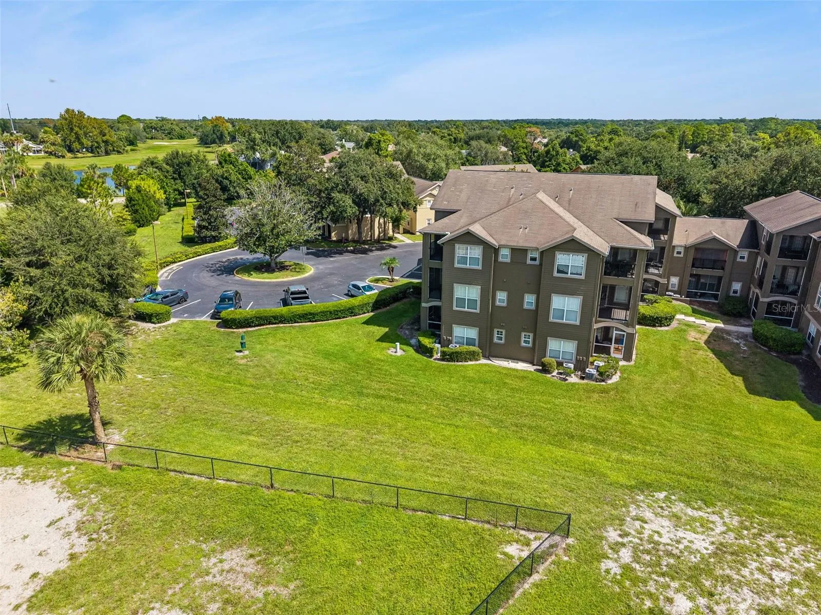 Aerial view of the three-story building with a landscaped lawn, circular parking area, trees, and golf course beyond.