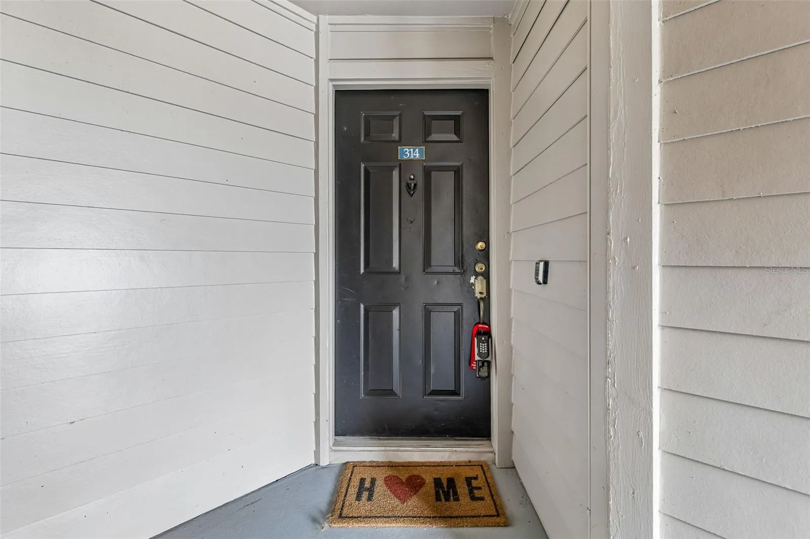 Front door of Unit 314 on a covered exterior landing, with the unit number above the door and a welcome mat.