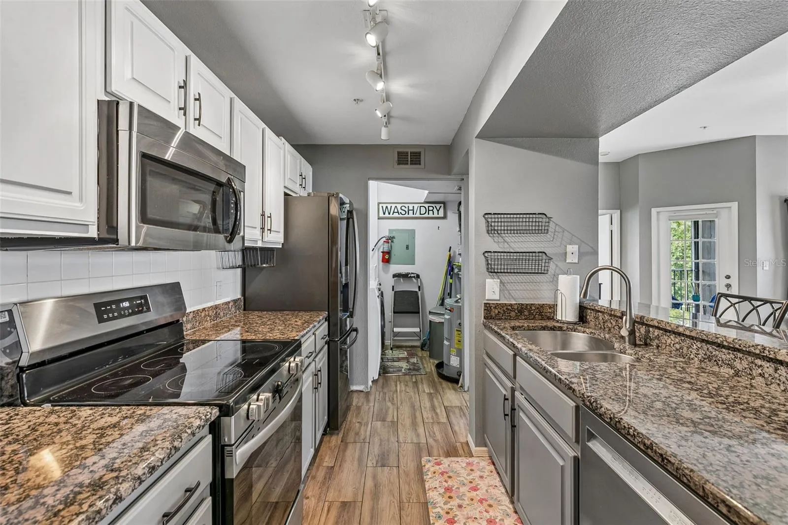Galley kitchen with granite countertops, white cabinets, stainless steel range and microwave, black refrigerator, double sink, and a laundry closet at the far end.