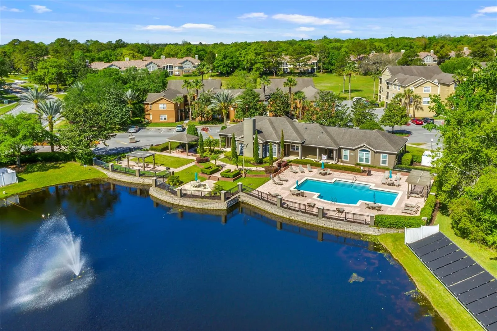 Aerial view of the Sabal Point clubhouse and pool beside the lake with its fountain on a clear day.