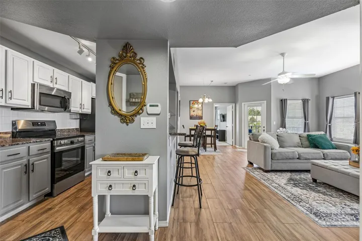 Open floor plan viewed from the kitchen entry, showing the living room and dining area with gray walls, ceiling fans, and ceramic tile  wood-look plank flooring.