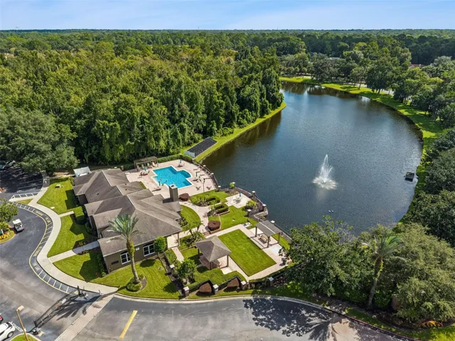 Aerial view of the Sabal Point clubhouse entrance, curved drive, and lakefront pool area with a fountain in the lake.