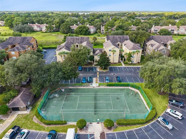 Sabal Point tennis court with green playing surface and fencing, next to a parking area and residential buildings.