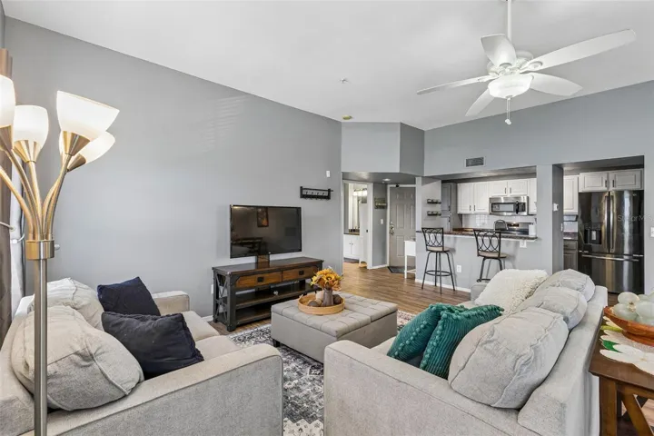 Living room looking toward the kitchen, with the breakfast bar, stainless appliances, and entry foyer visible in the background.
