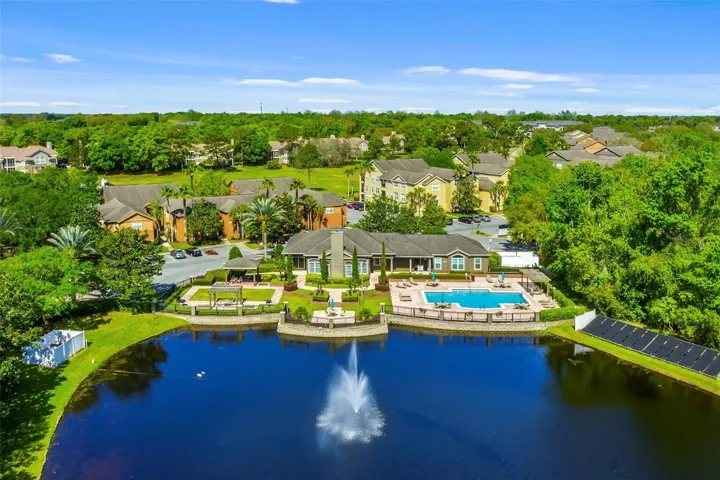 Wide aerial view of the Sabal Point lake with fountain, clubhouse, pool, and nearby residential buildings.