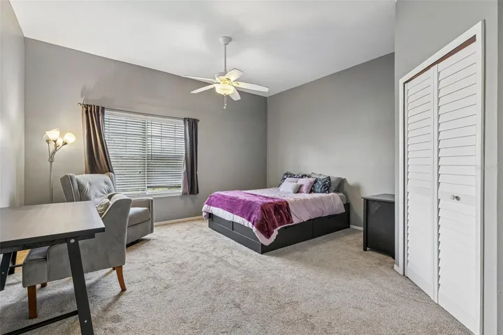 Second bedroom with carpeted floor, ceiling fan, window, louvered double-door closet, and bed.