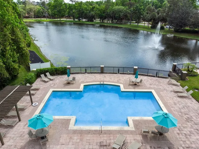 Sabal Point pool and deck beside the lake, with lounge chairs, umbrellas, black fencing, and a lake fountain in the distance.
