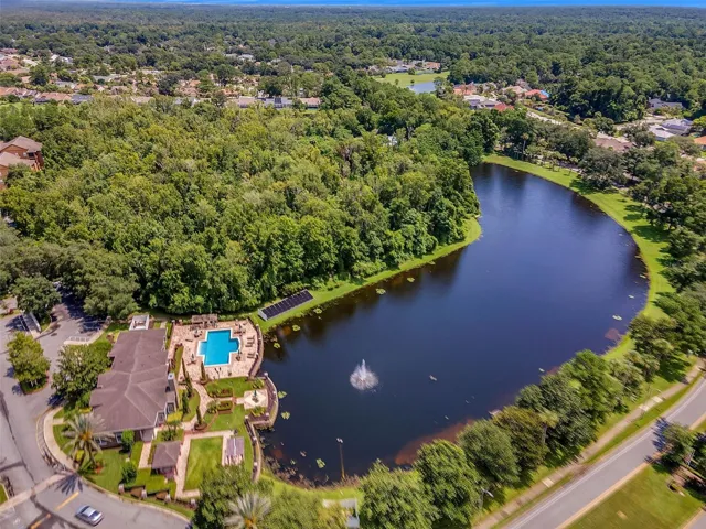 Wide aerial view of the Sabal Point lake with a fountain, wooded shoreline, clubhouse, and pool.