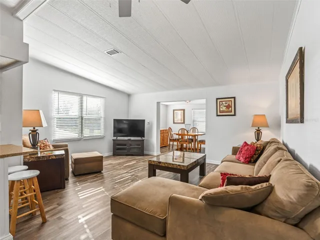 View of LIVING ROOM from Dining Area - Shows CATHEDRAL CEILING and abundant NATURAL LIGHT from large windows in the front of the home. Note opening to BONUS / FLEX SPACE in back center.