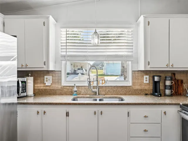 KITCHEN Close-Up View - REFRIGERATOR (far L), Countertop MICROWAVE (back L), White cabinets, GRANITE COUNTERTOPS, TILE BACKSPLASH, Undermount dual basin SS SINK w/ PULL DOWN FAUCET, PENDANT LIGHTING over sink, and SS ELECTRIC RANGE (far R).