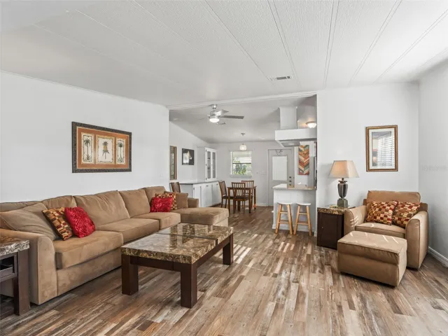 Another view of LIVING ROOM - Shows CATHEDRAL CEILING running longitudinally - front to back of home. DINING ROOM (back L), FRONT DOOR ENTRANCE (center back), and KITCHEN (back R).