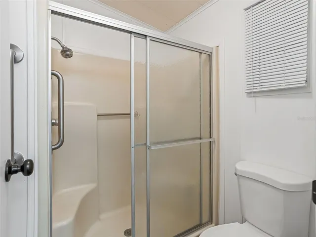 View of WALK-IN SHOWER w/ SLIDING GLASS DOORS and COMFORT HEIGHT TOILET (R). Note SAFETY BARS located outside and inside of WALK-IN SHOWER.