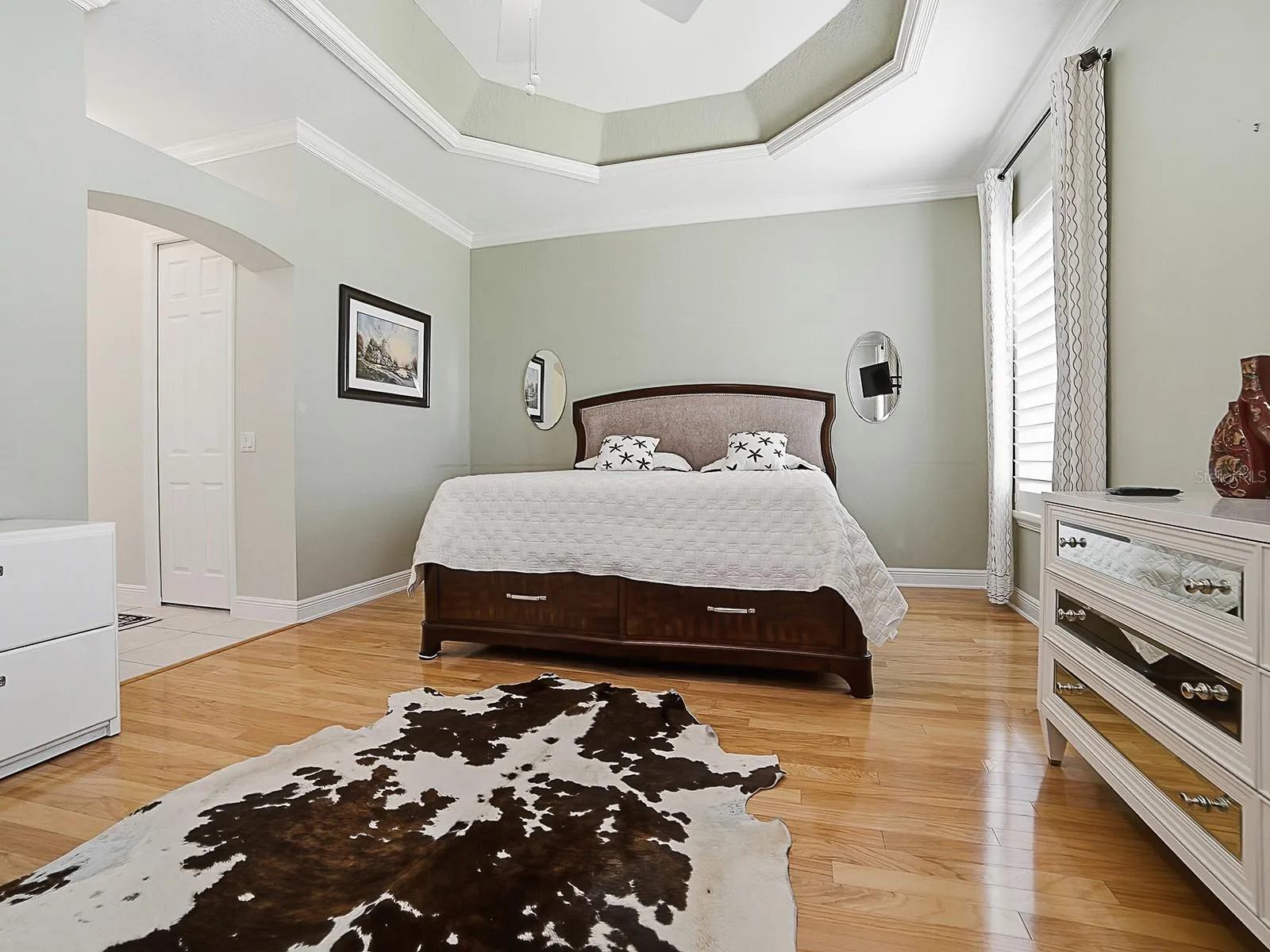 PRIMARY BEDROOM WITH TRAY CEILING, CROWN MOLDING, AND THOSE BEAUTIFUL HARDWOOD FLOORS.