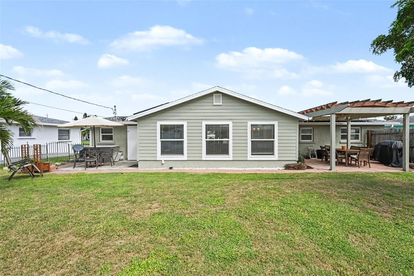 Spacious backyard featuring a green lawn, concrete patio, and a wooden pergola at 412 Redwood Road, Venice, Florida