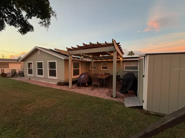 Sunset view of the outdoor living space featuring a paver patio and a wooden pergola illuminated by string lights at 412 Redwood Road, Venice, Florida