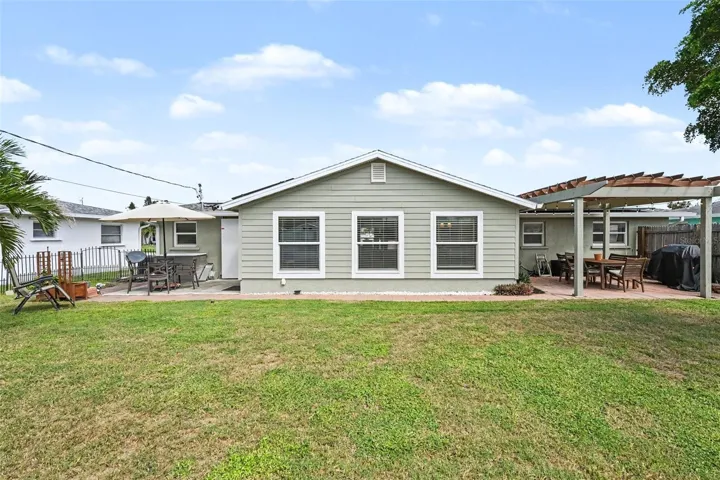 Spacious backyard featuring a green lawn, concrete patio, and a wooden pergola at 412 Redwood Road, Venice, Florida