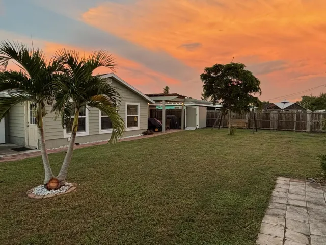 Colorful sunset view over the spacious fenced backyard and palm trees at 412 Redwood Road, Venice, Florida