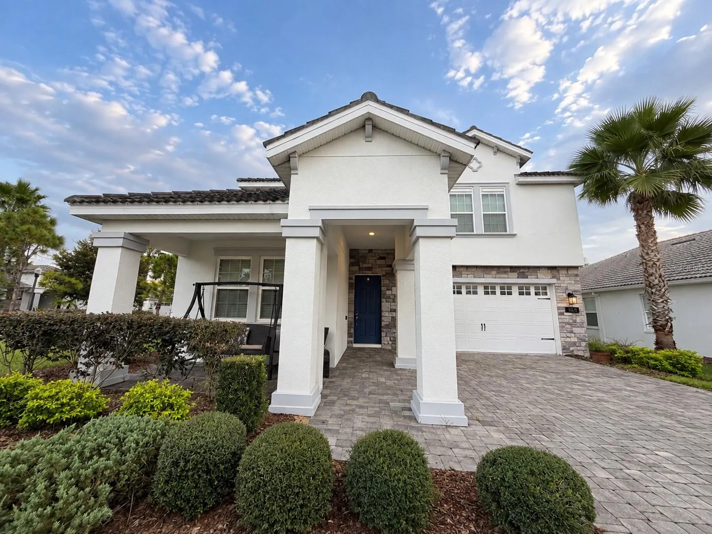Inviting front elevation featuring a covered porch, stone accents and paver driveway.