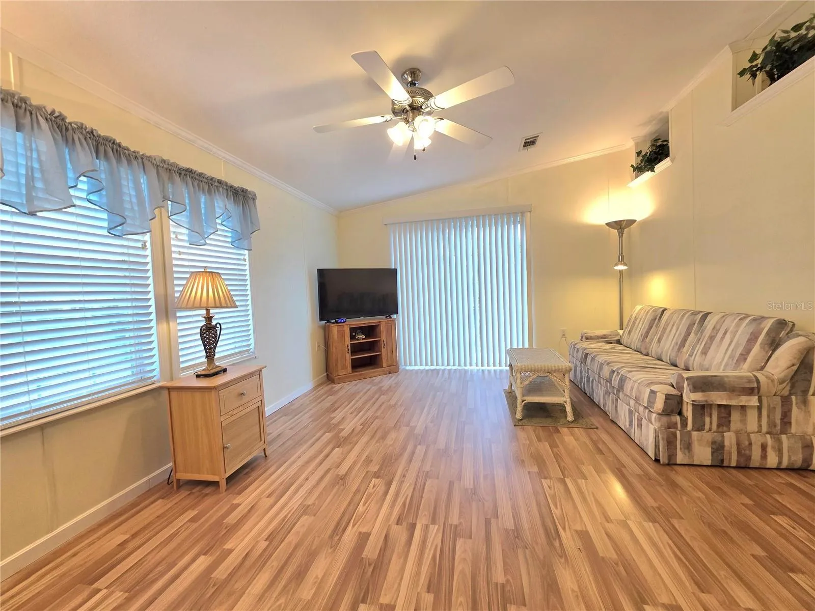 Living room with sliding glass door, ceiling fan, &amp; built in plant shelves.