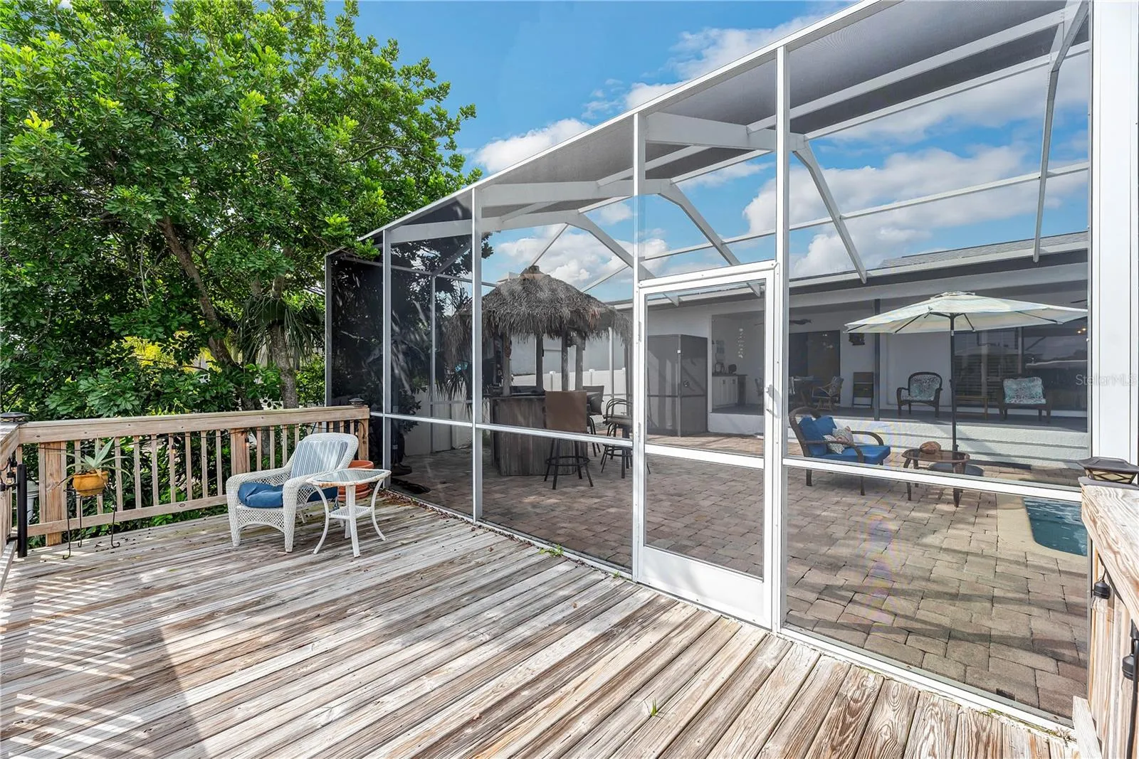 A spacious, open-air wooden deck just beyond the pool cage extends the outdoor entertaining area.
