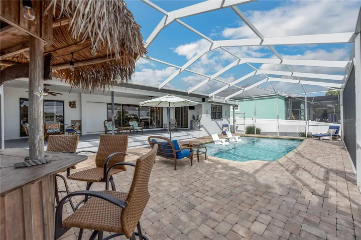 screened outdoor retreat featuring a heated saltwater pool, Tiki bar and spacious pavered deck.