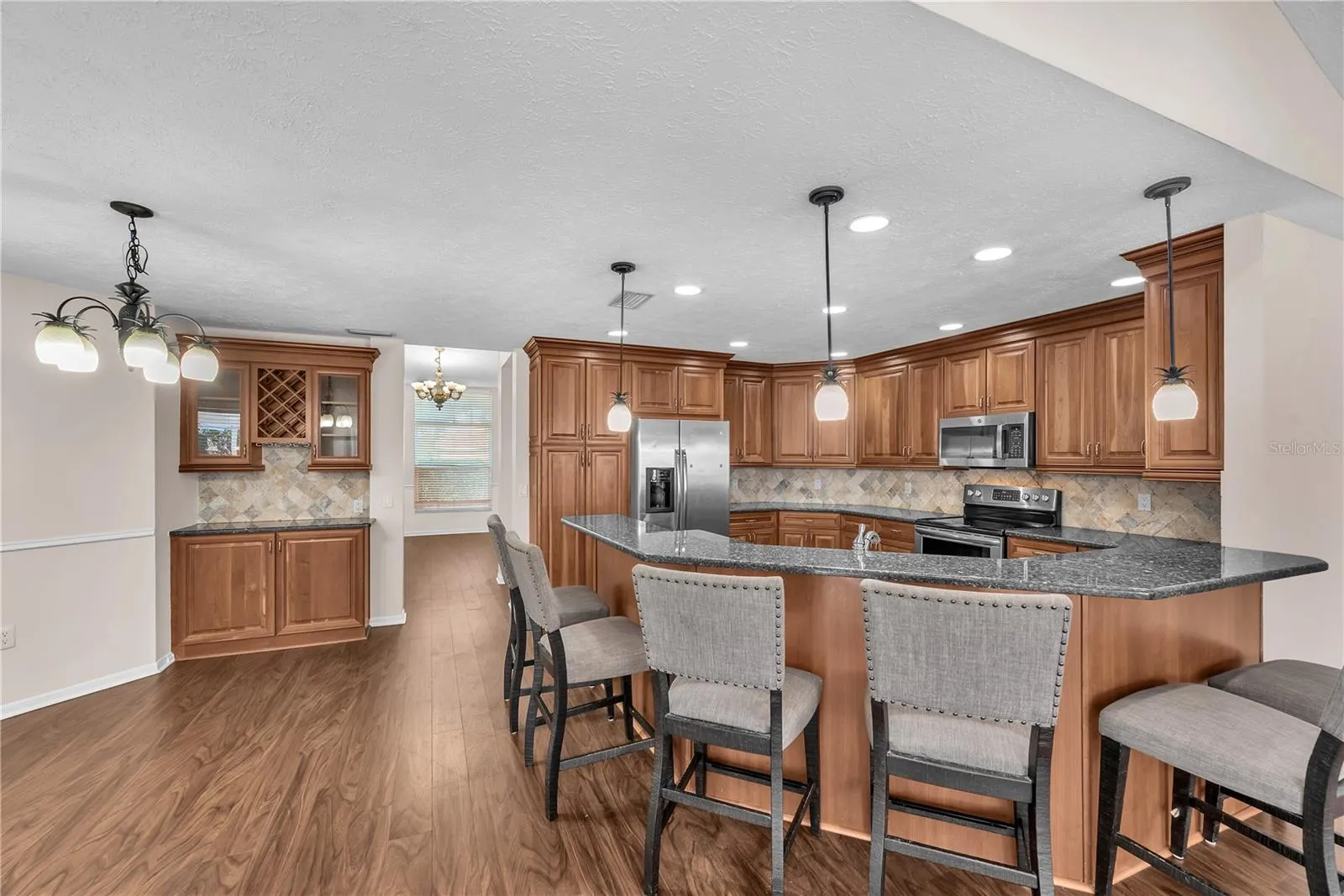 The breakfast bar provides additional seating, while a wall of cabinetry with a built-in wine rack and glass-front doors offers the perfect spot for displaying serving pieces and setting out appetizers for guests or creating a convenient coffee station.