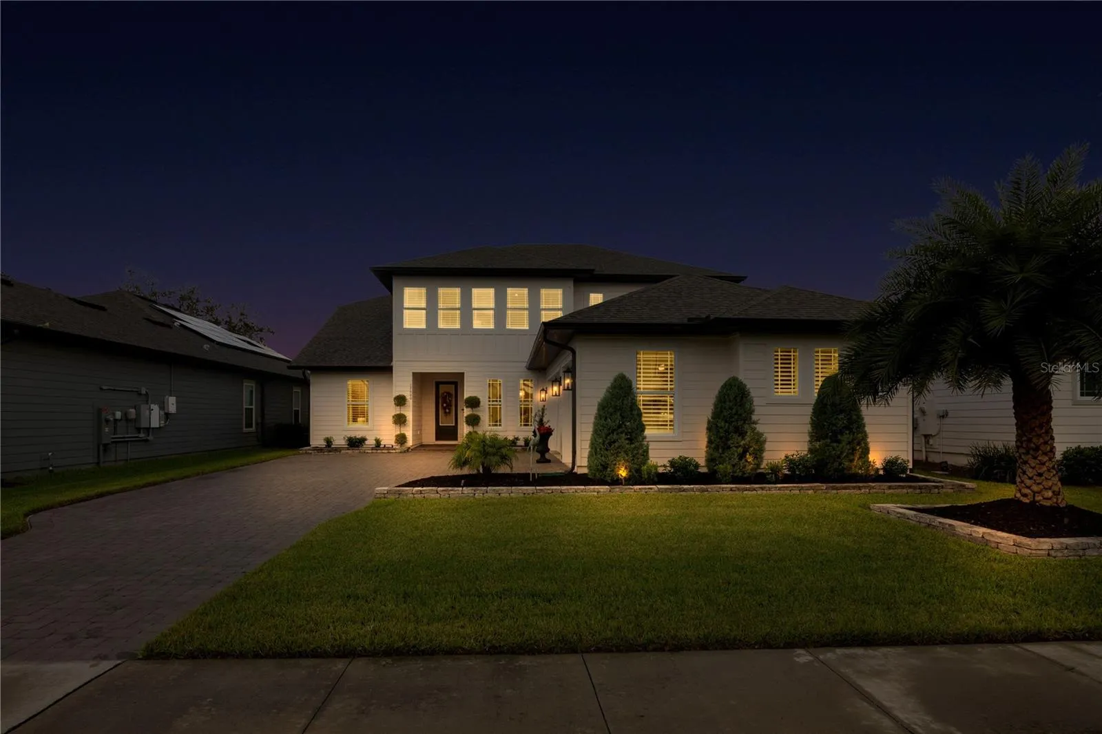 Twilight view of the paver driveway and front entrance with warm exterior lighting.