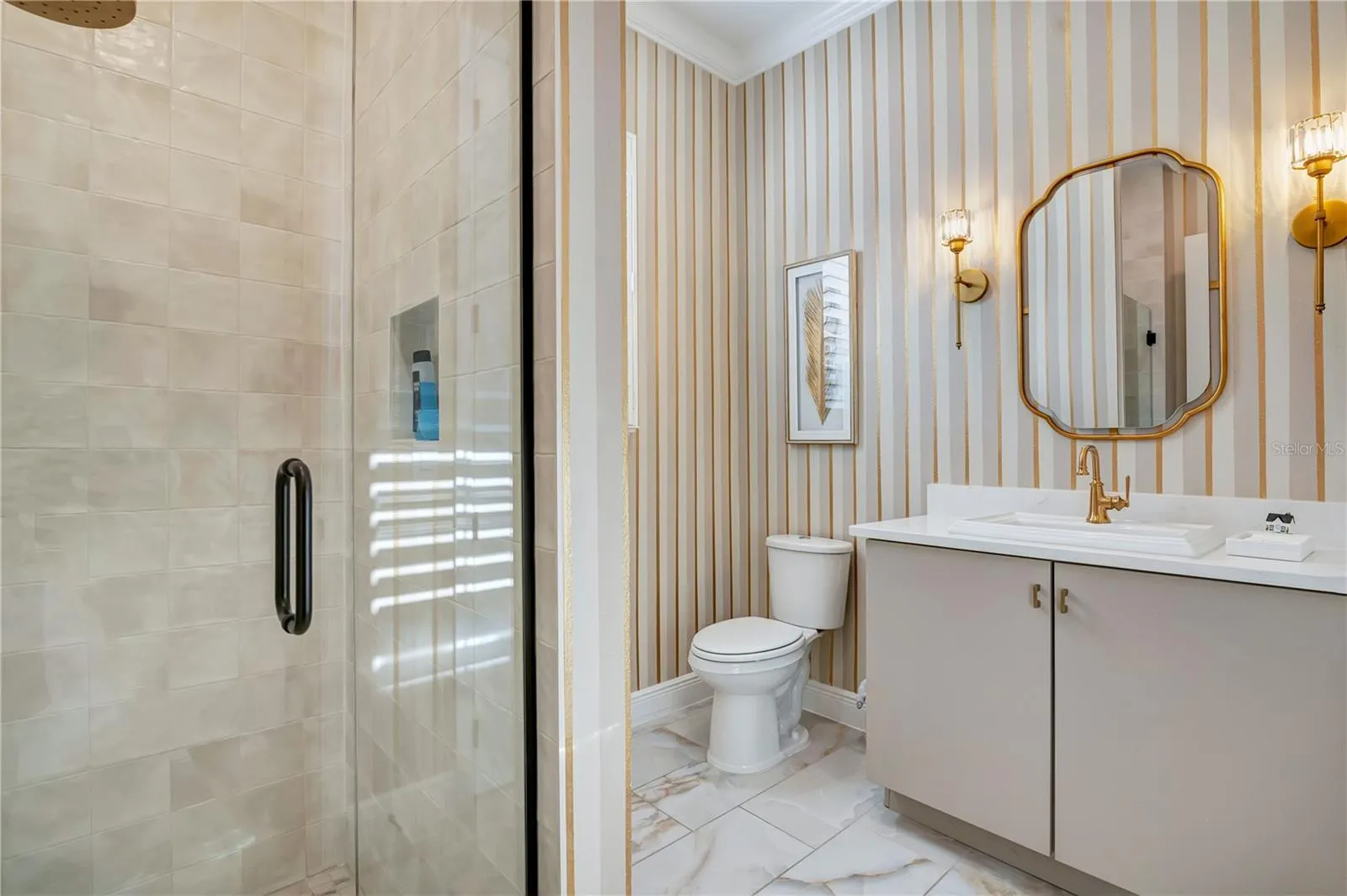 Designer bathroom with a glass-enclosed shower, striped accent wall and gold-tone fixtures.