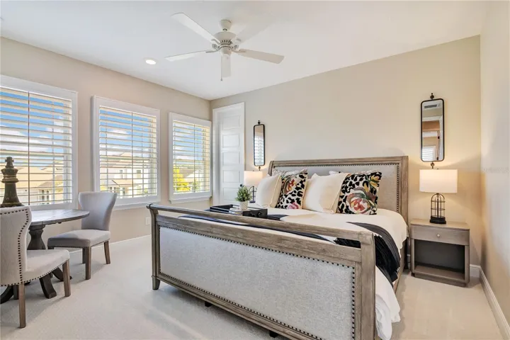 Inviting bedroom featuring plush carpet, plantation shutters and a ceiling fan.