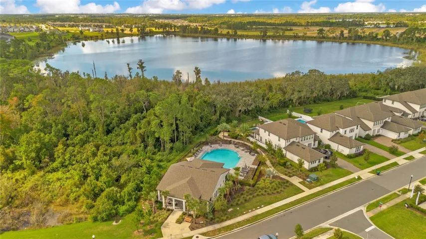 Aerial view of the community amenity area with a pool, clubhouse and lake backdrop.