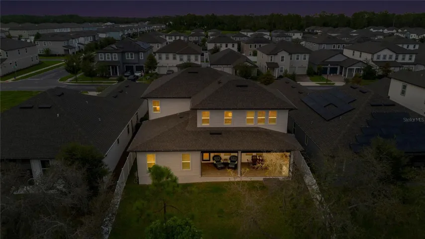 Rear aerial at twilight captures the backyard and warmly illuminated covered lanai.