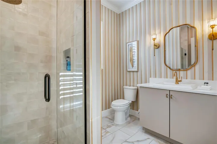 Designer bathroom with a glass-enclosed shower, striped accent wall and gold-tone fixtures.