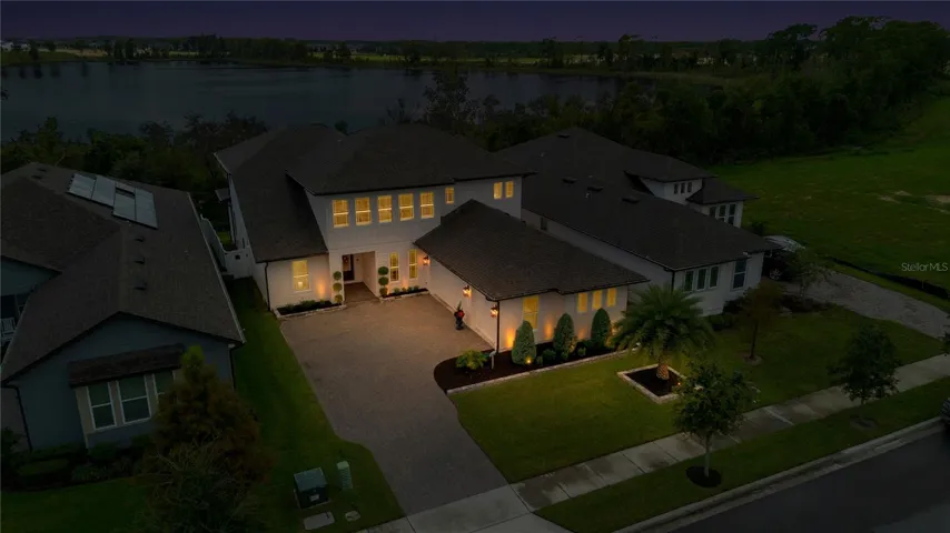 Twilight aerial showcases the home with the lake visible beyond the surrounding trees.