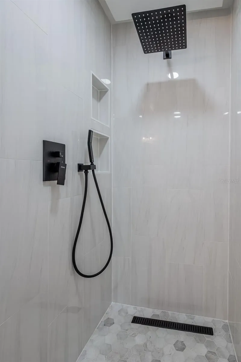 Completely gutted and rebuilt in 2022 with an investment of approximately $32,000, the primary bathroom includes a floating quartz double vanity, illuminated mirrors, an oversized walk in rain shower, multiple shower fixtures and lighted niches.