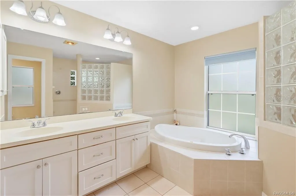 Primary Bathroom – Spacious ensuite featuring a dual-sink vanity, large mirror, soaking jetted tub and tile flooring.