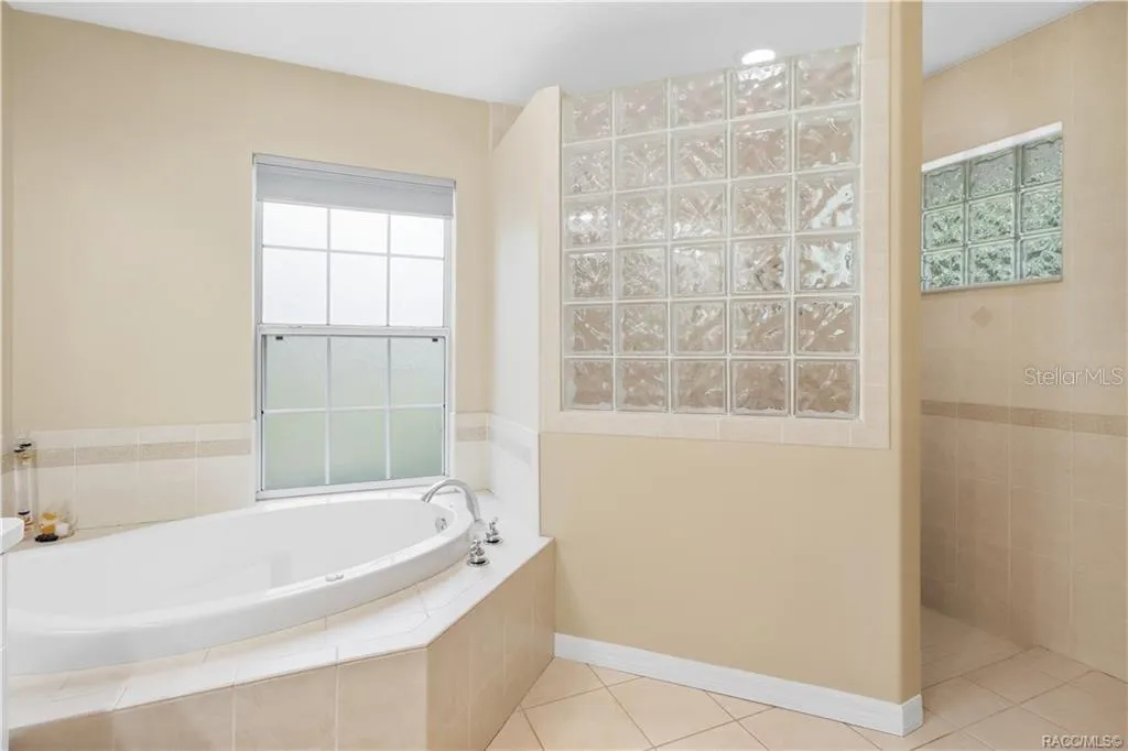 Primary Bathroom – Alternate view showcasing the soaking tub, decorative glass-block accents and separate tiled walk-in shower.